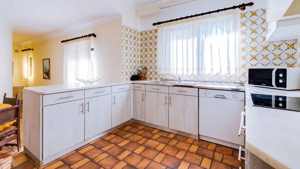 A bright kitchen with white cabinets and a tiled floor.