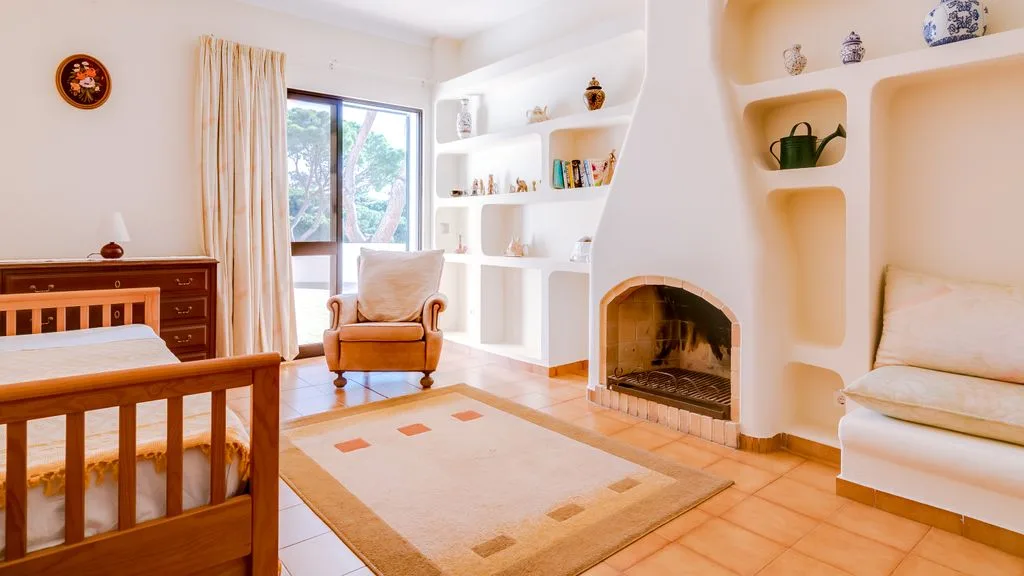A bright bedroom with a wooden bed, armchair, and built-in shelves.