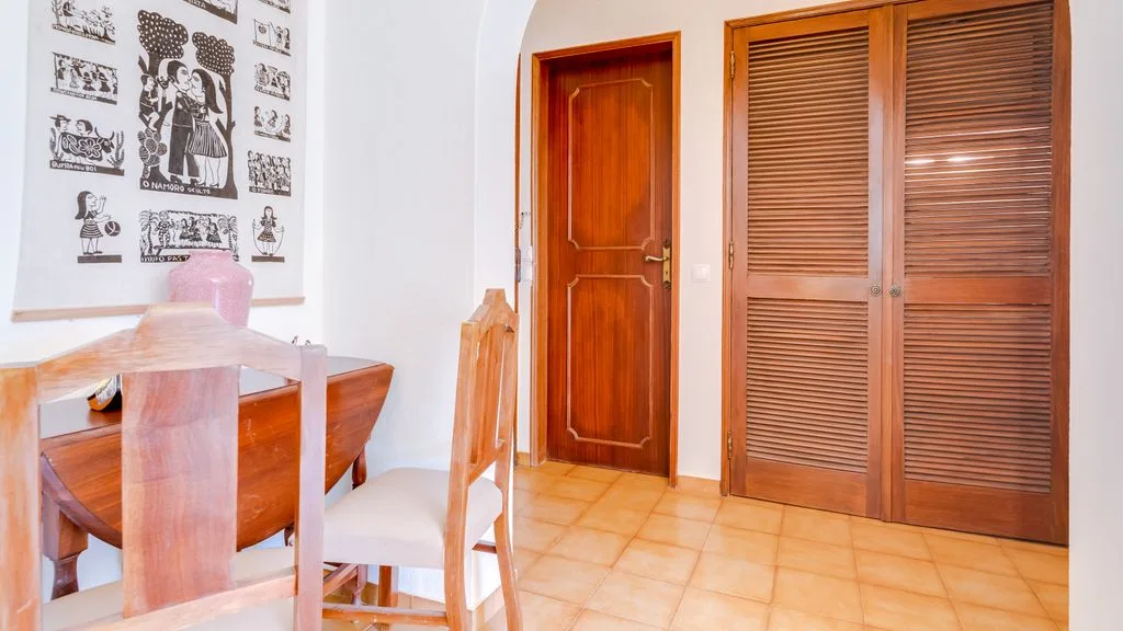 A dining area with a wooden table beside a door and louvered closet doors.