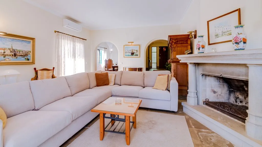 A bright living room with pale seating, a coffee table, and a fireplace.