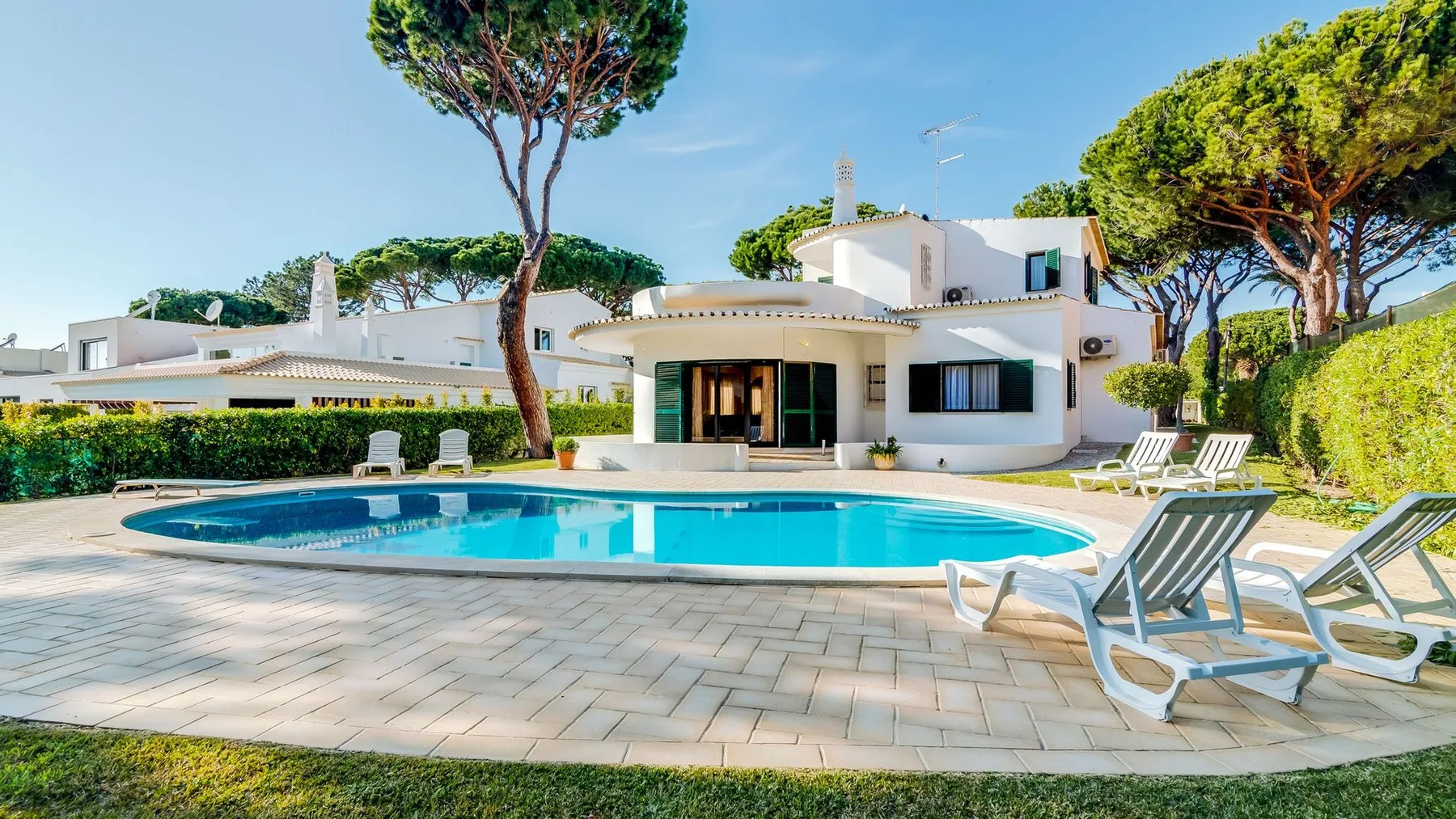 A modern white house overlooks a swimming pool and paved patio.