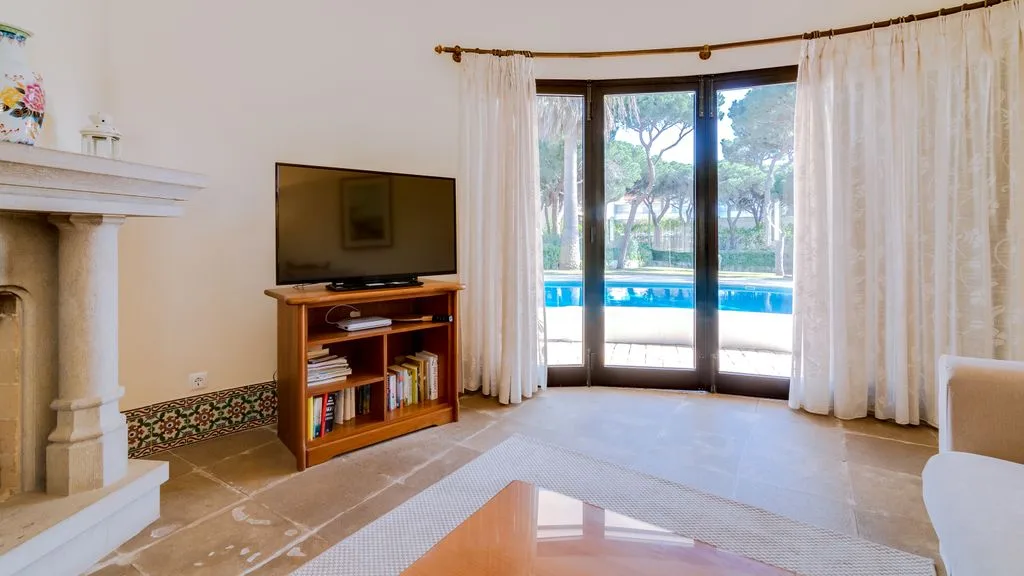 A living room with a television and glass doors opening onto a pool.