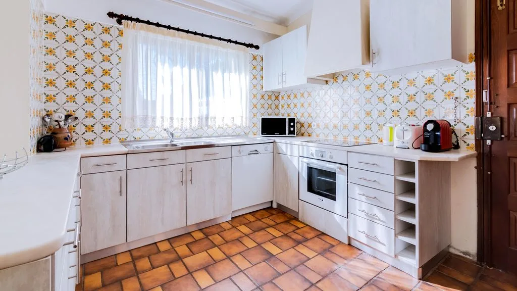 A kitchen with light cabinets, tiled walls, and a window above the sink.