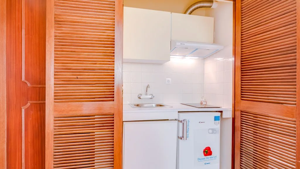 A compact kitchen with white cabinets and a refrigerator between wooden louvered panels.
