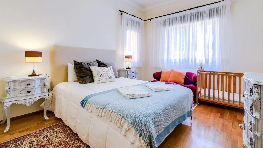 A bedroom with a bed, bedside tables, and large curtained windows.