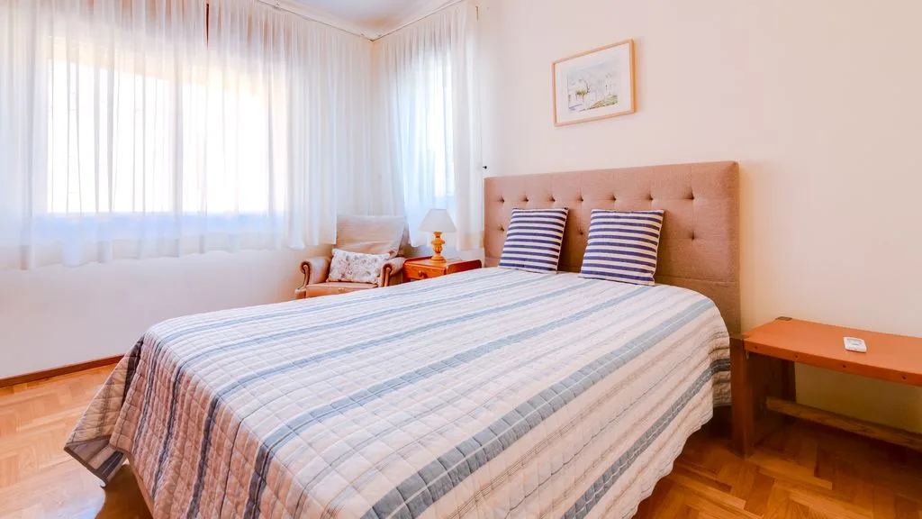 A bedroom with a bed, striped bedding, and sheer curtains.