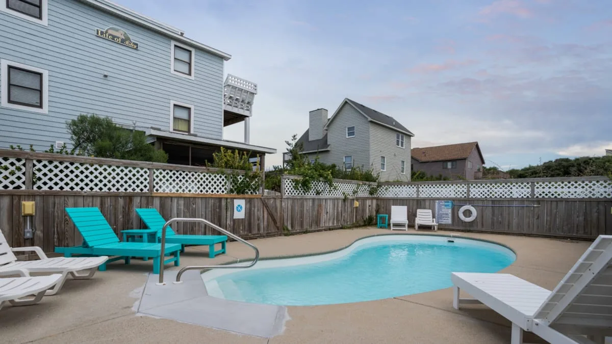 An outdoor swimming pool sits beside deck chairs and neighboring houses.