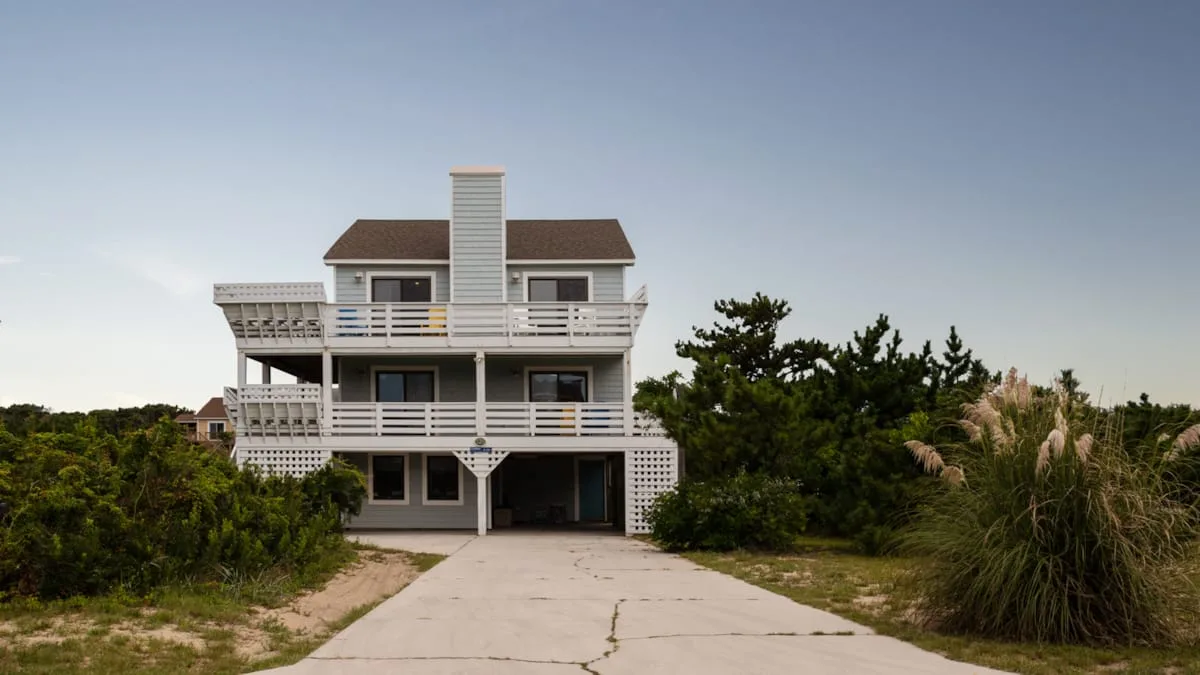 A raised coastal-style house stands at the end of a broad driveway.