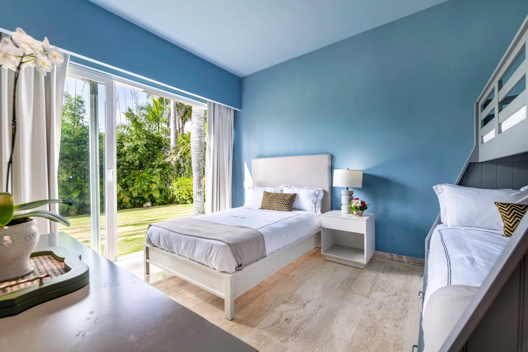 Un dormitorio luminoso con una cama junto a grandes ventanales con vistas a la vegetación.