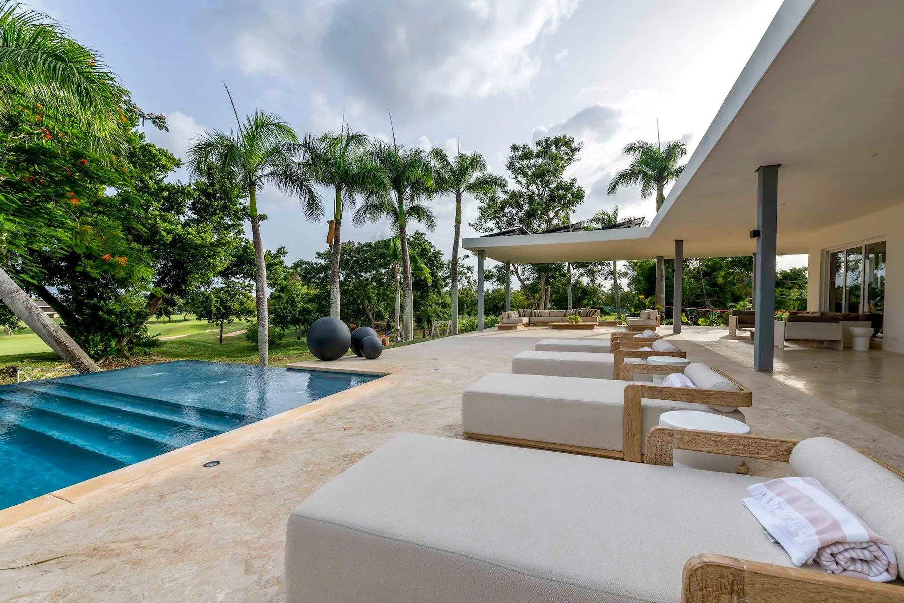 Una zona de descanso junto a la piscina, con asientos acolchados bajo un patio cubierto.