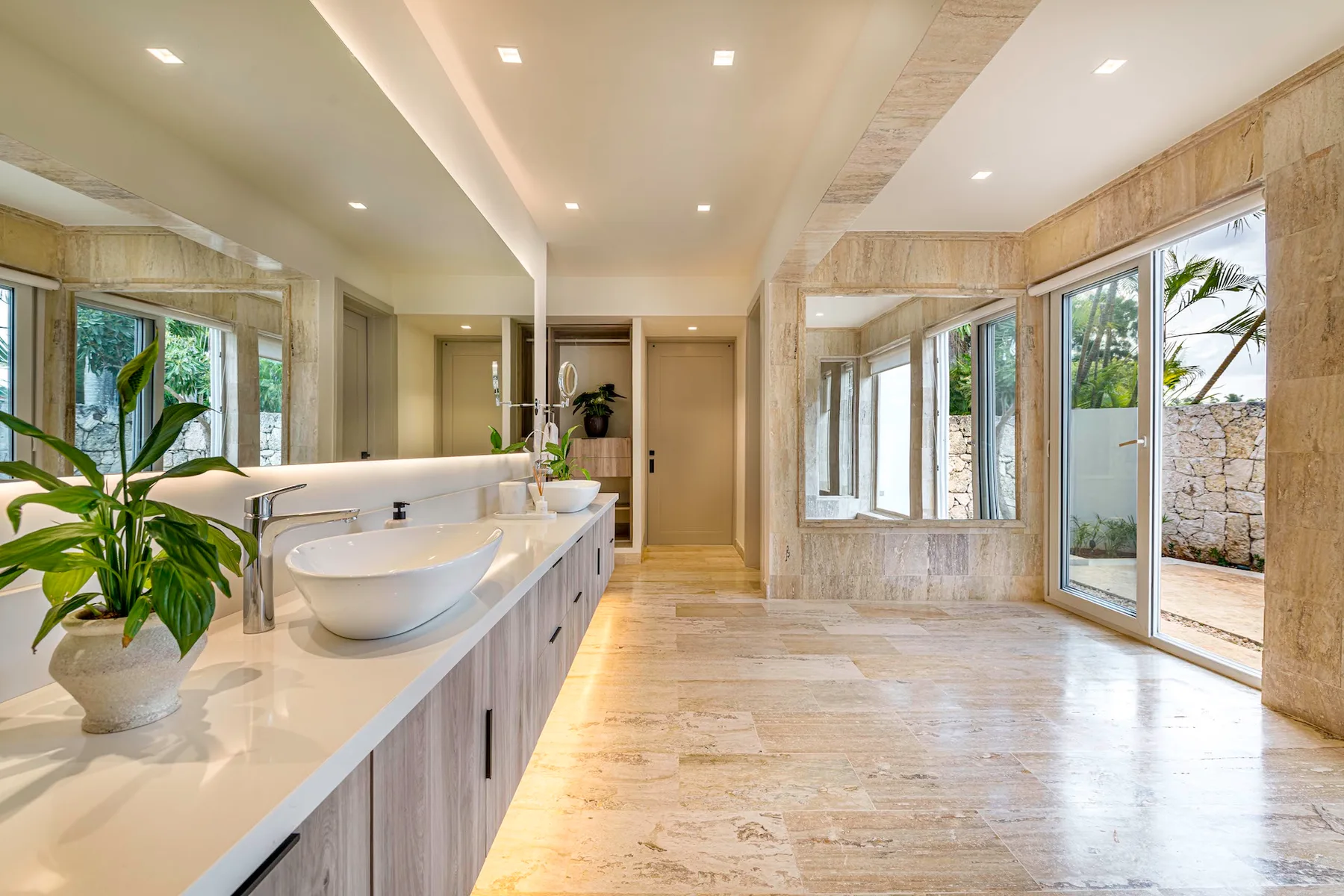 Un baño luminoso con un tocador largo y grandes ventanas hacia el jardín.