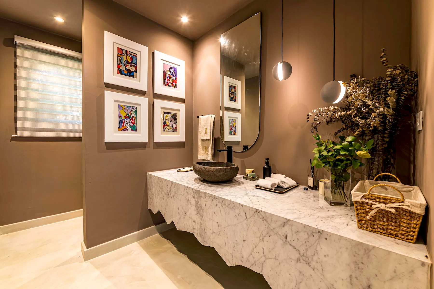 Un tocador de baño con luz cálida, obras enmarcadas y un lavabo sobre encimera.