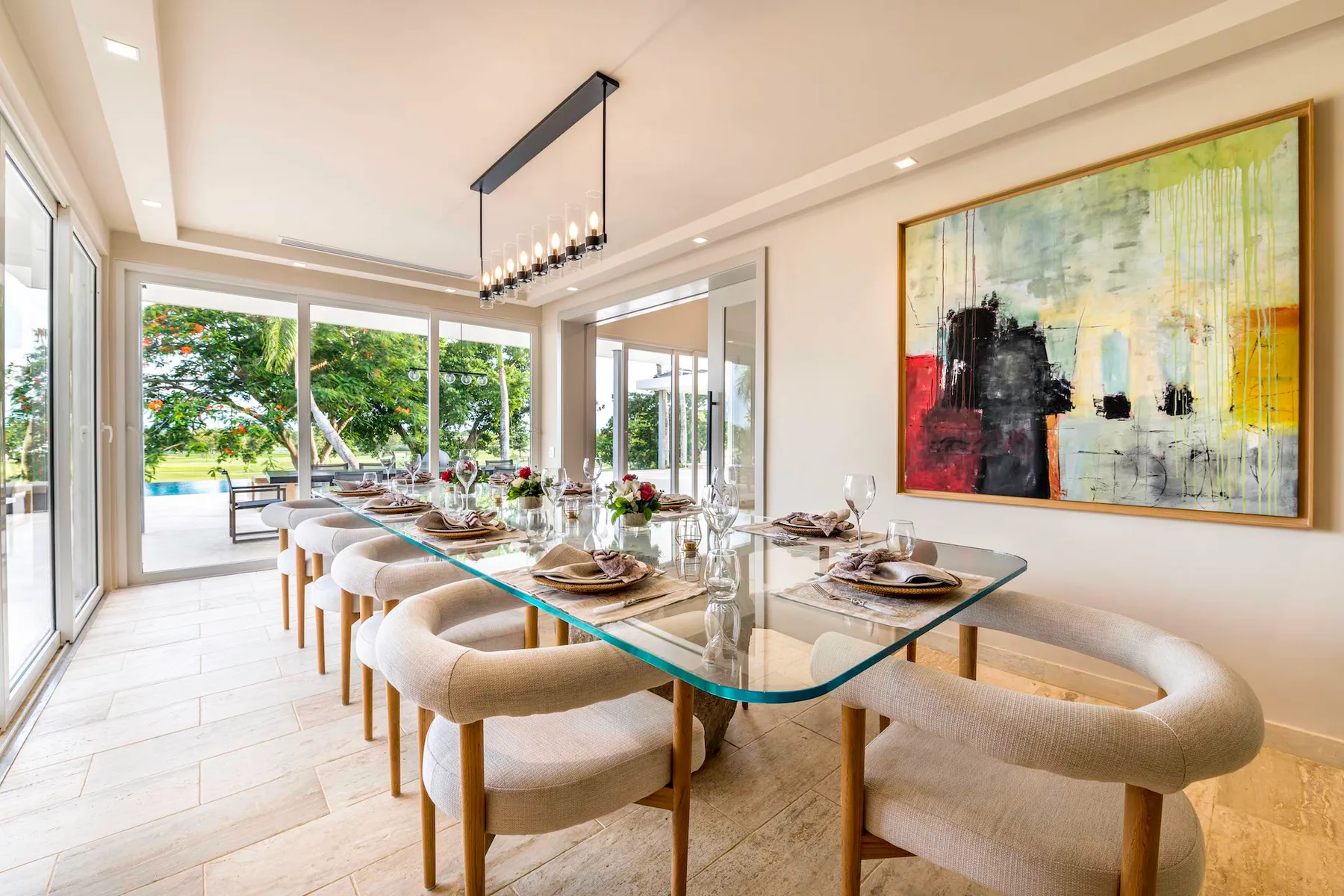 Un comedor luminoso con una mesa larga de vidrio y grandes ventanales con vistas a la vegetación.
