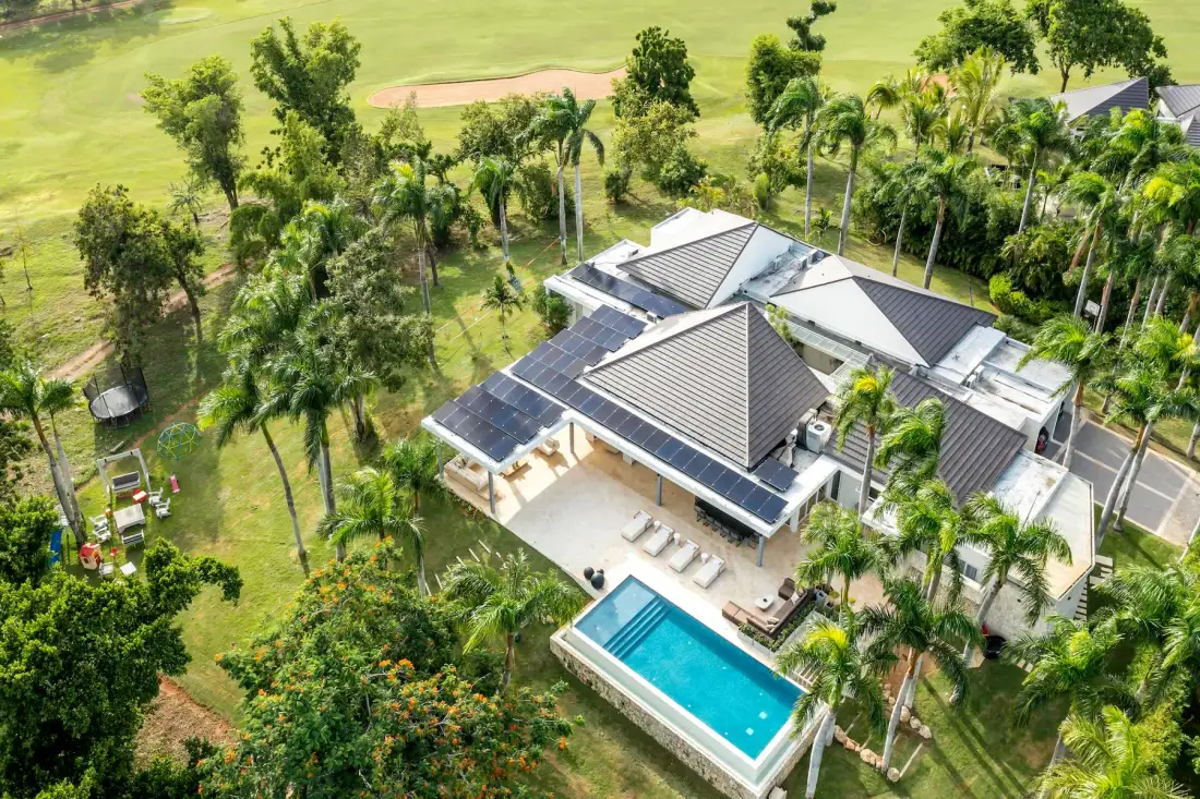 Vista aérea de una casa moderna con piscina entre jardines verdes.