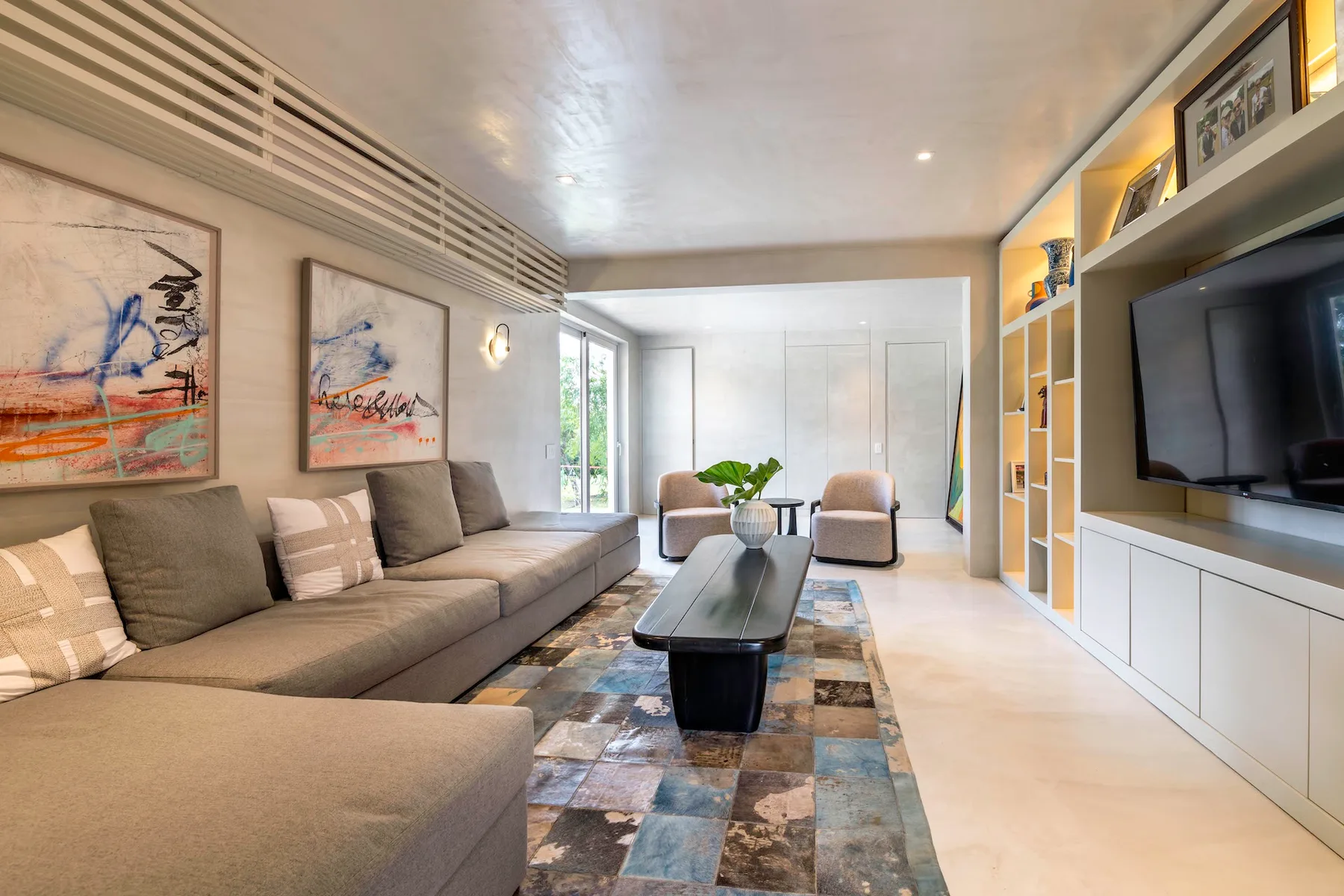 Una sala luminosa tiene asientos seccionales, una mesa de centro y un televisor en la pared.