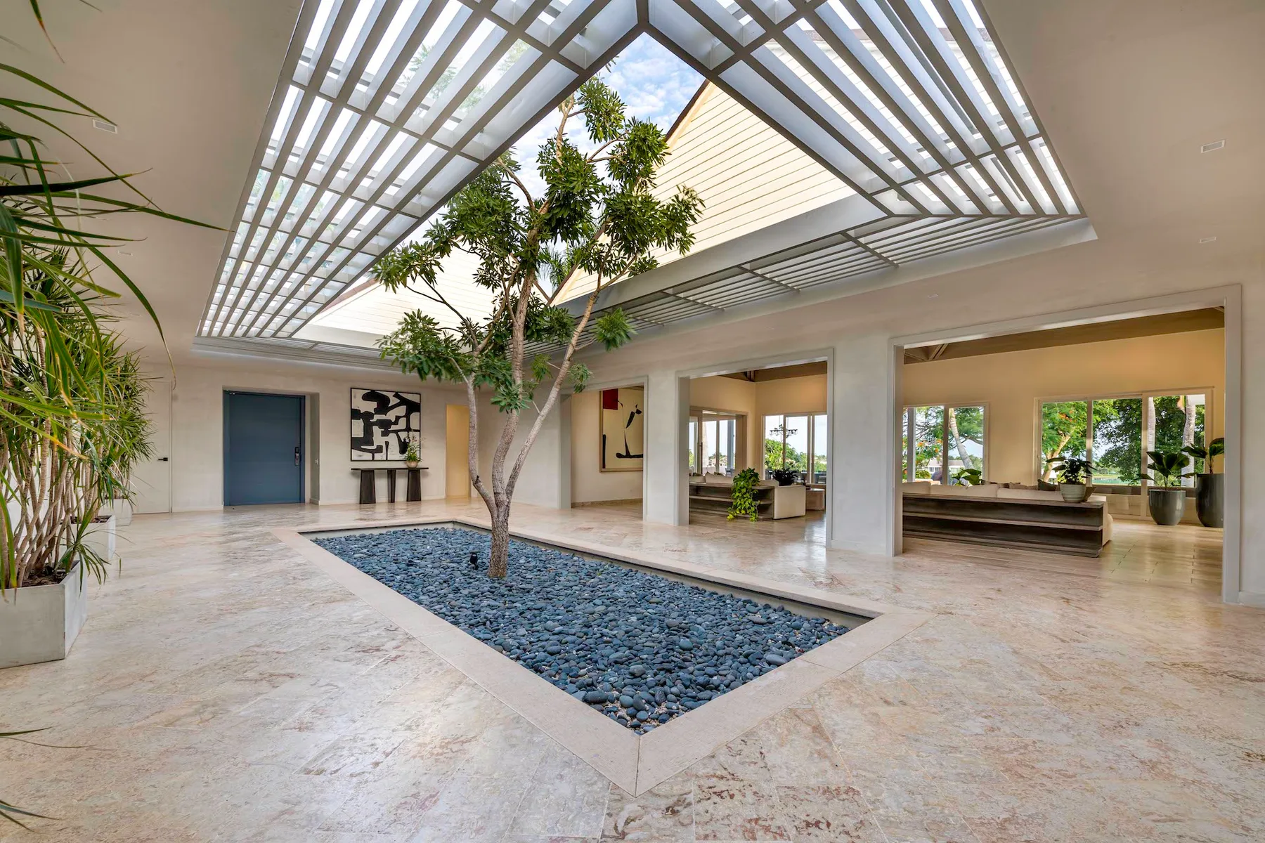Un patio interior luminoso con un árbol junto a un largo lecho de piedras oscuras.