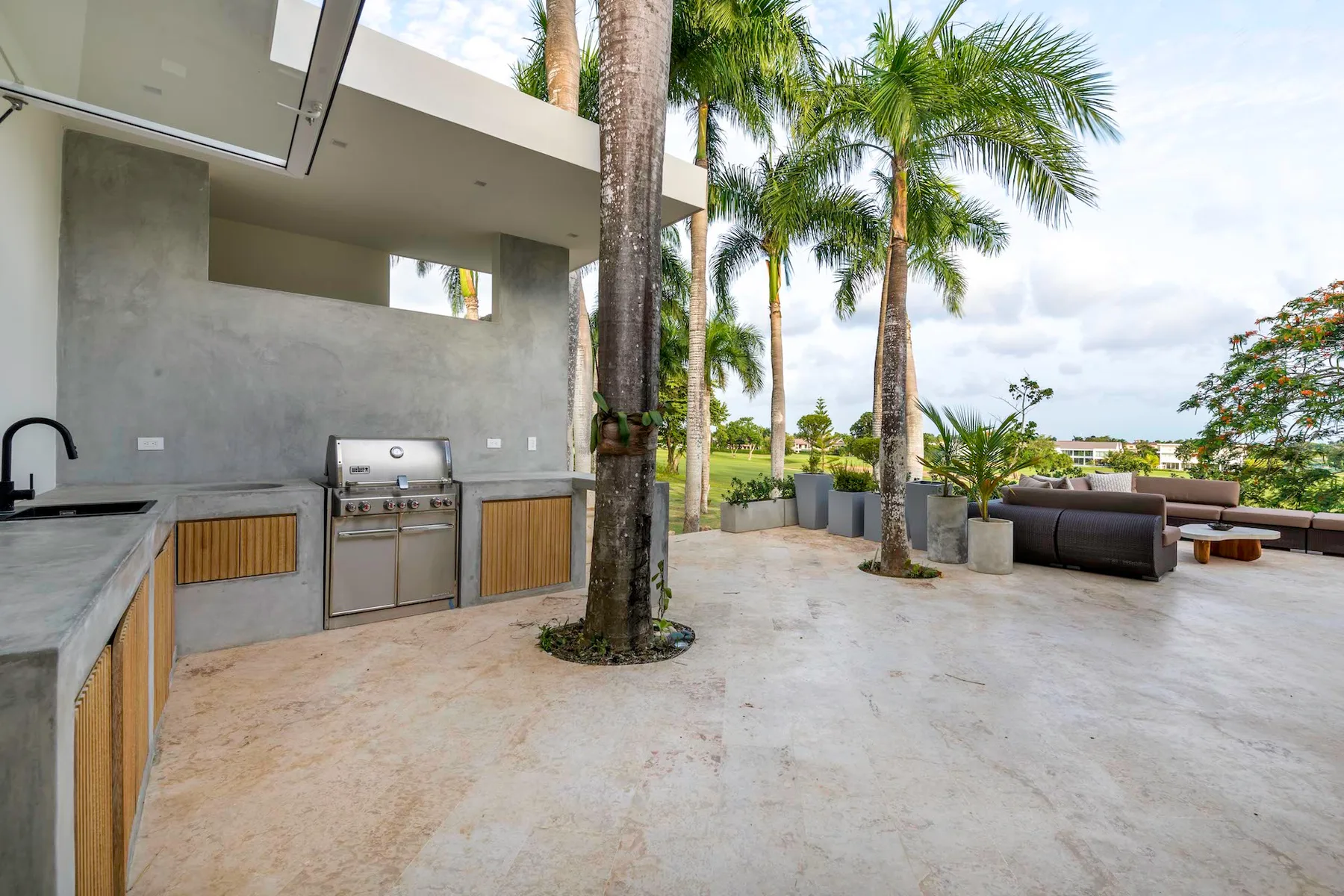 Una cocina exterior y una zona de estar dan a un jardín con palmeras.
