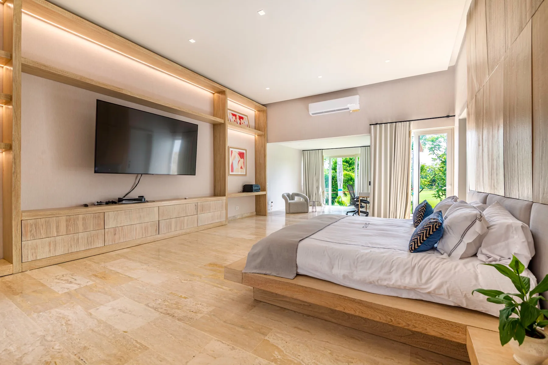 Un dormitorio luminoso con una cama grande, un televisor en la pared y puertas corredizas de vidrio.