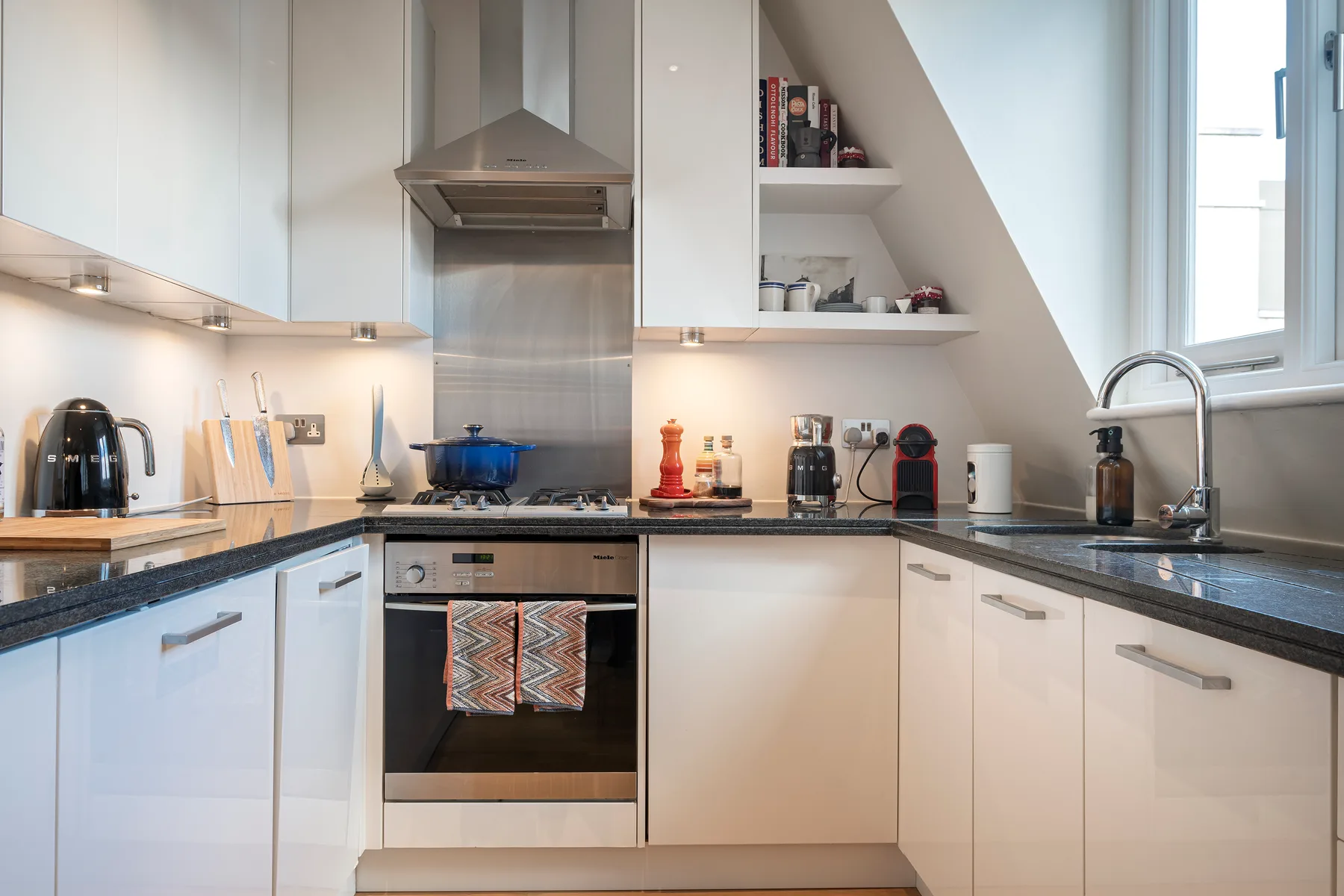 Una cocina luminosa con gabinetes blancos, encimeras oscuras y una campana extractora de acero inoxidable.