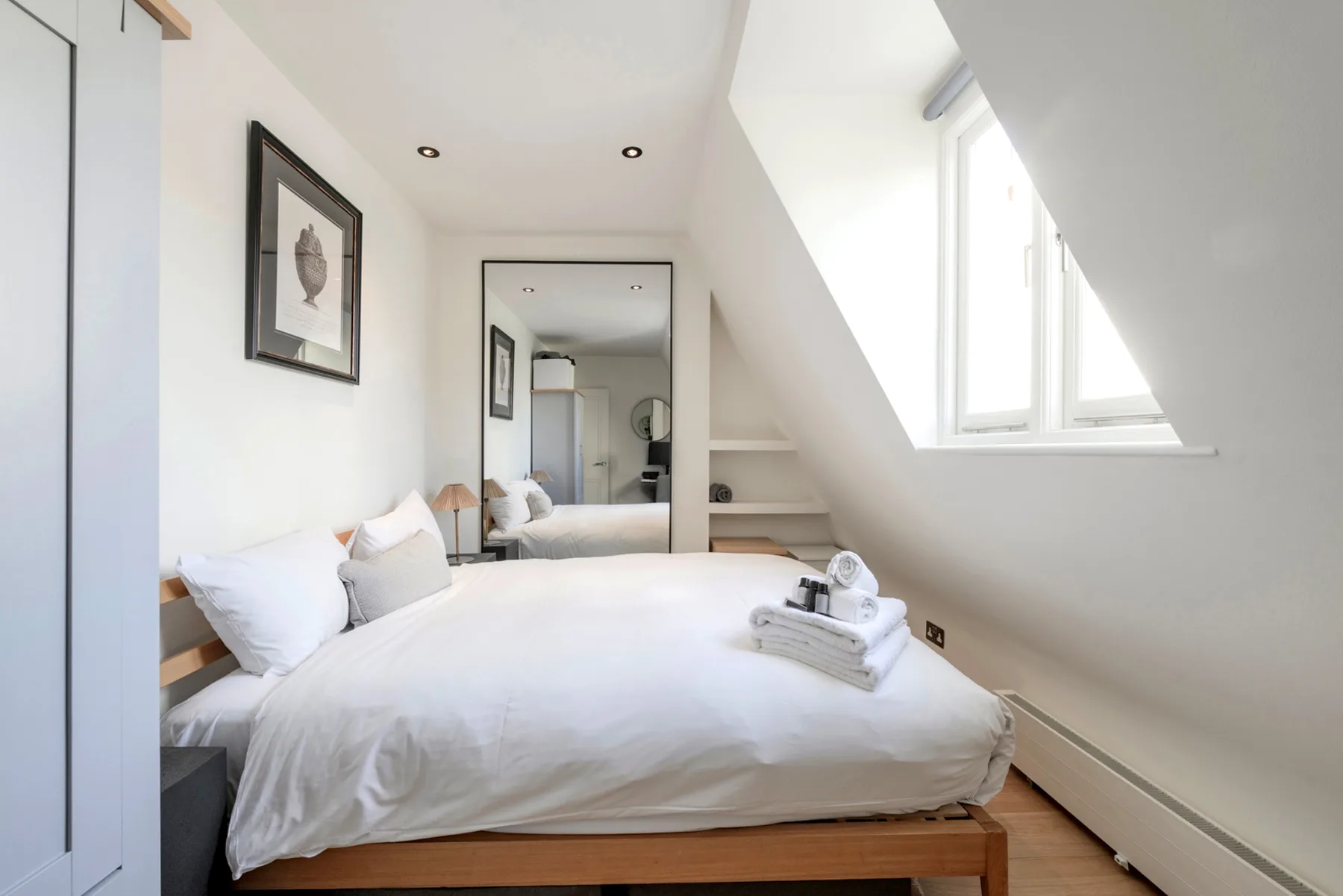 Un dormitorio luminoso con una cama bajo un techo inclinado y una ventana grande.