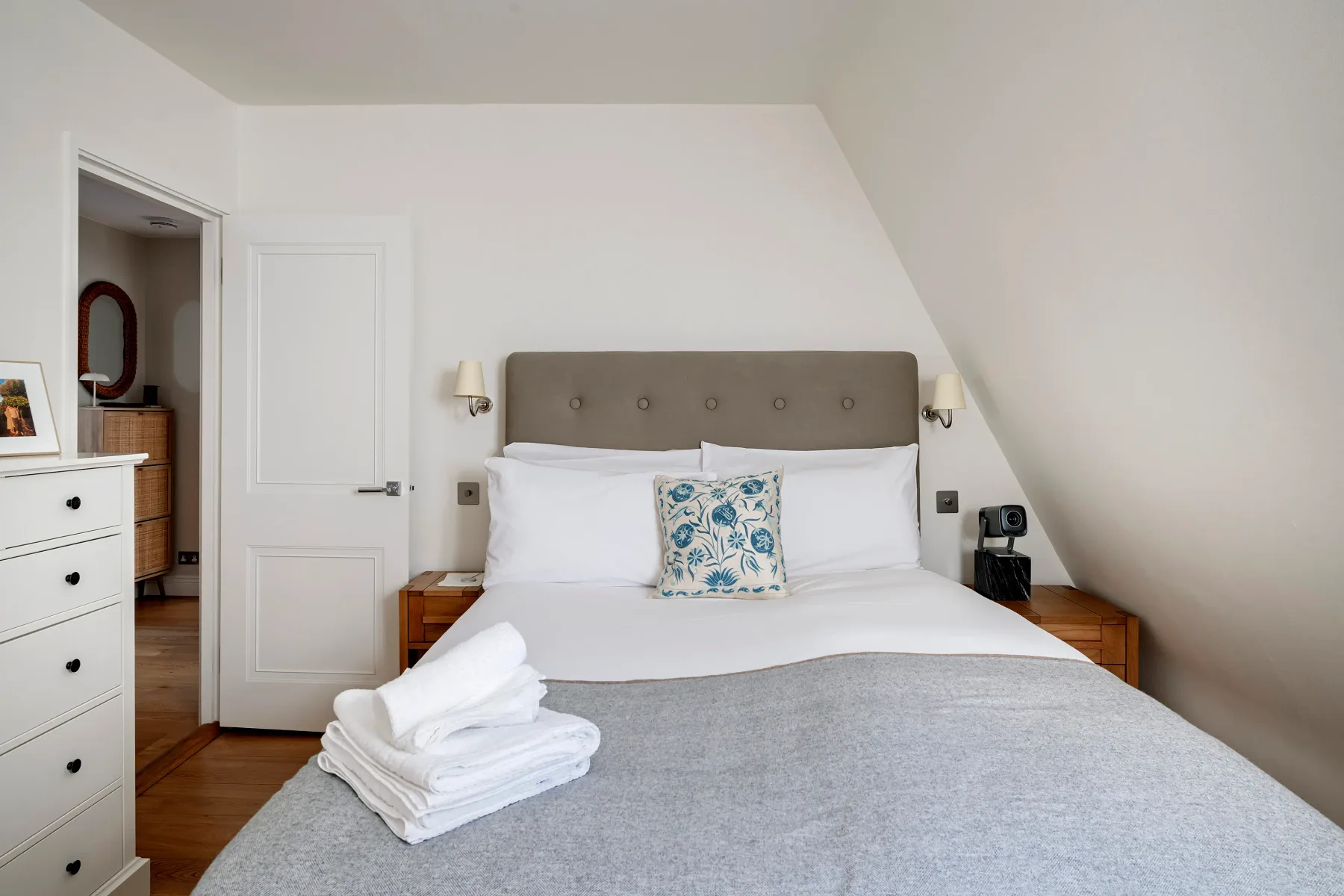 A bedroom with a double bed, gray headboard, and folded white towels.