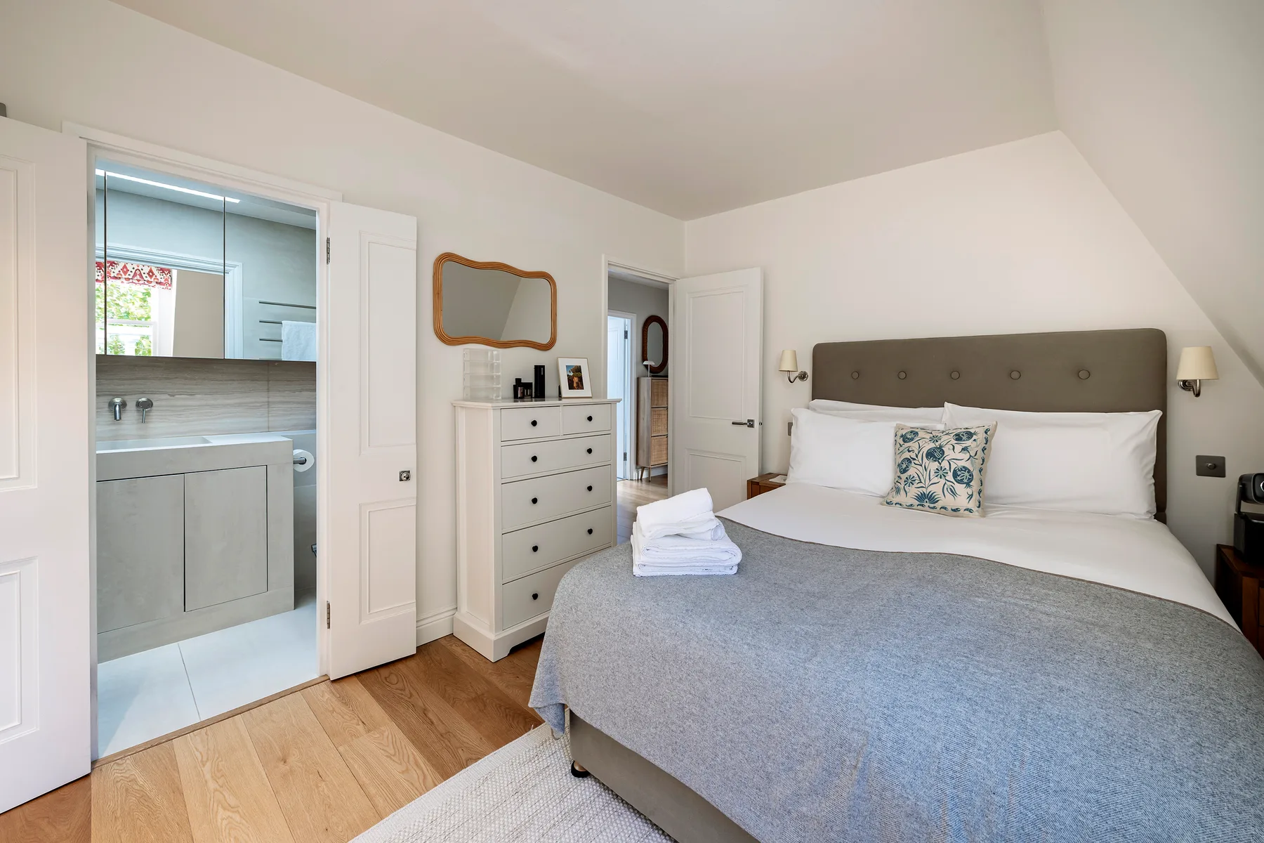 A bedroom with a neatly made bed and a dresser beside the bathroom.