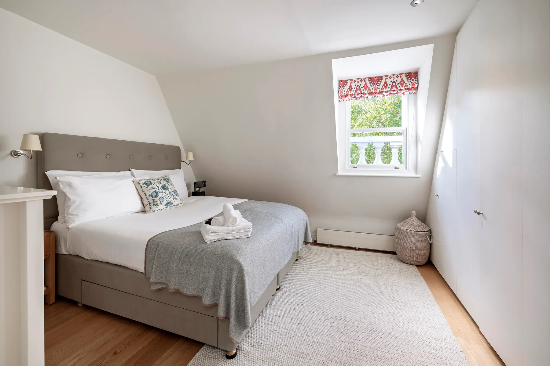 Un dormitorio luminoso con una cama bien hecha y una ventana con vistas a la vegetación.