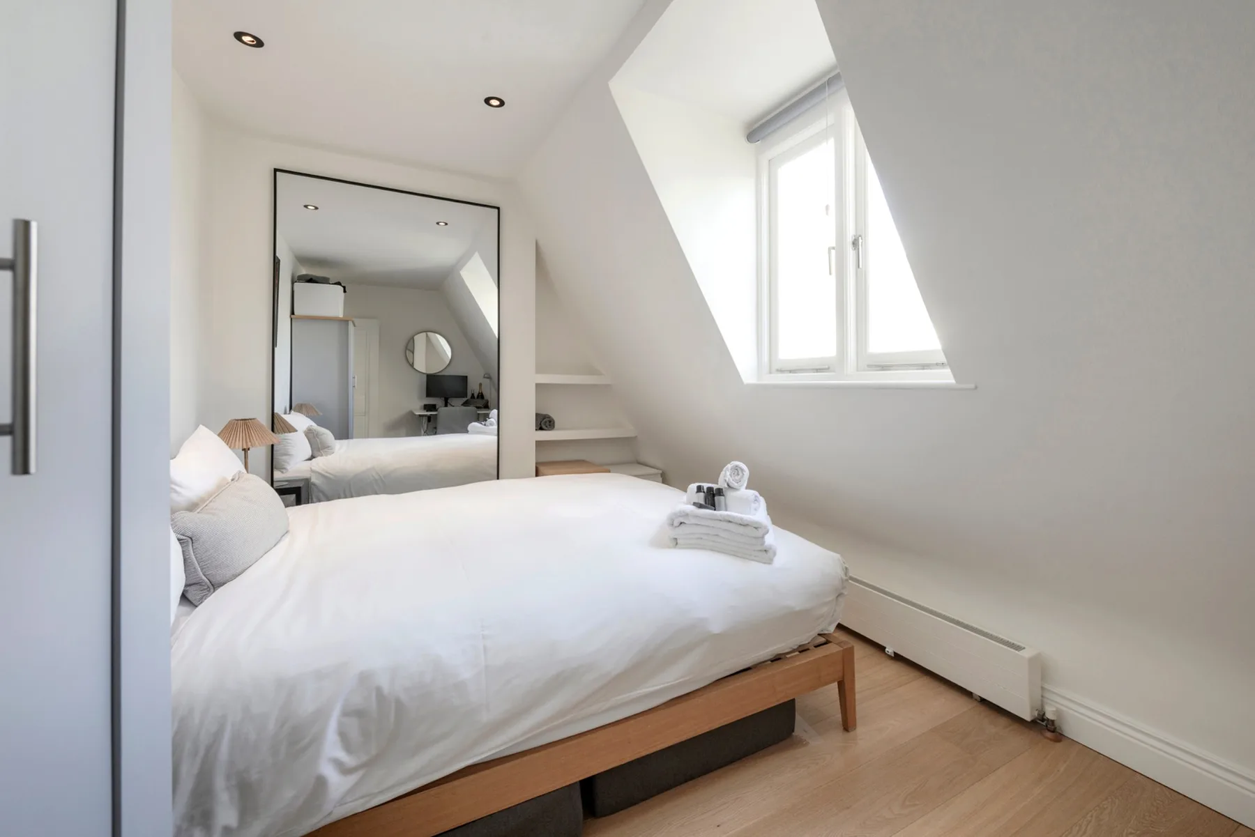 A bright attic bedroom with a white bed beneath a sloped ceiling.