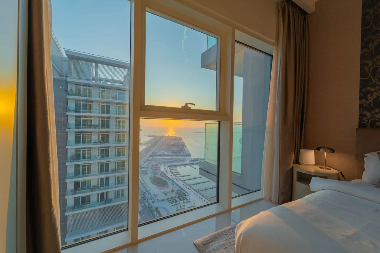 A bedroom with large windows overlooking the sea at sunset.