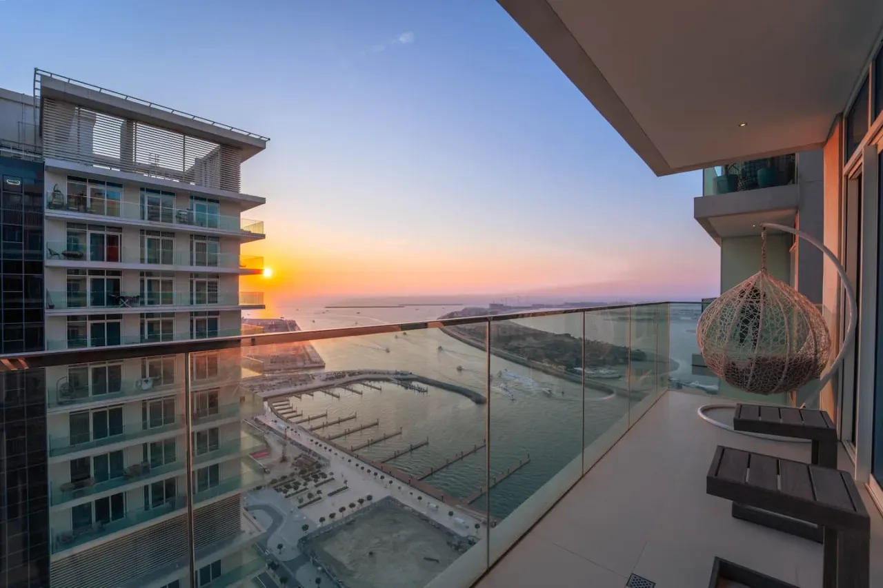 Un balcón ofrece vistas de edificios modernos y el océano al atardecer.