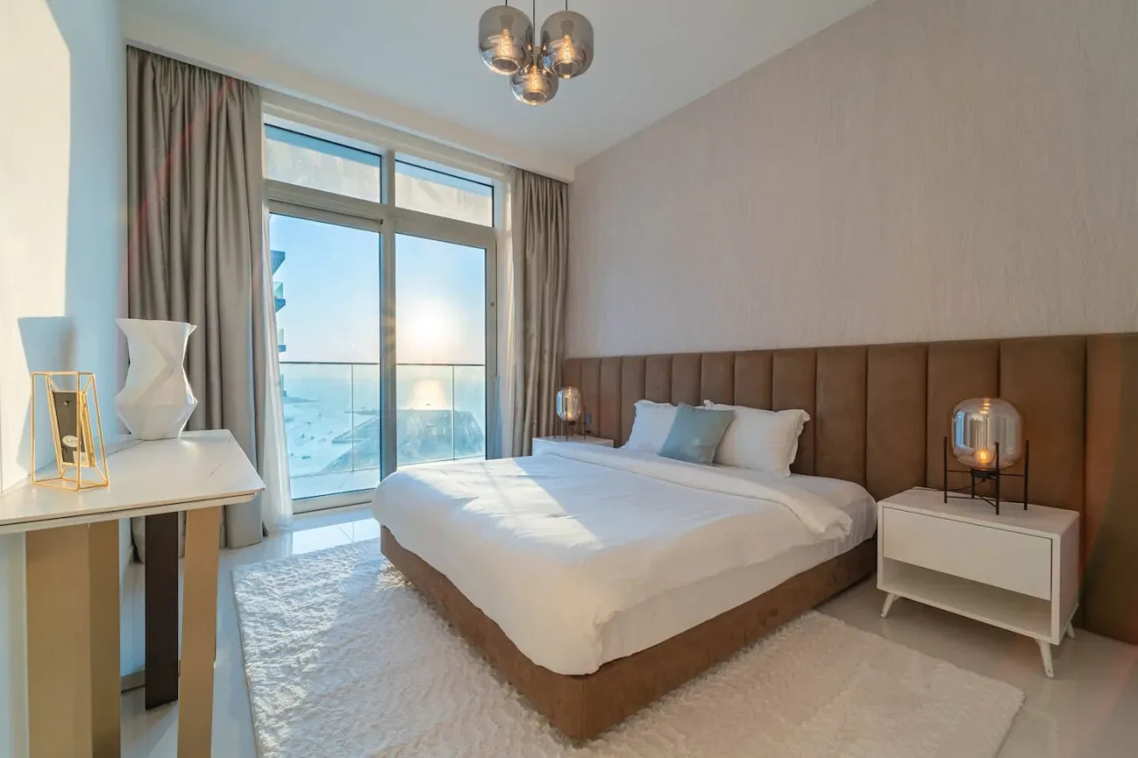 A bedroom with a bed beside tall windows overlooking a balcony.