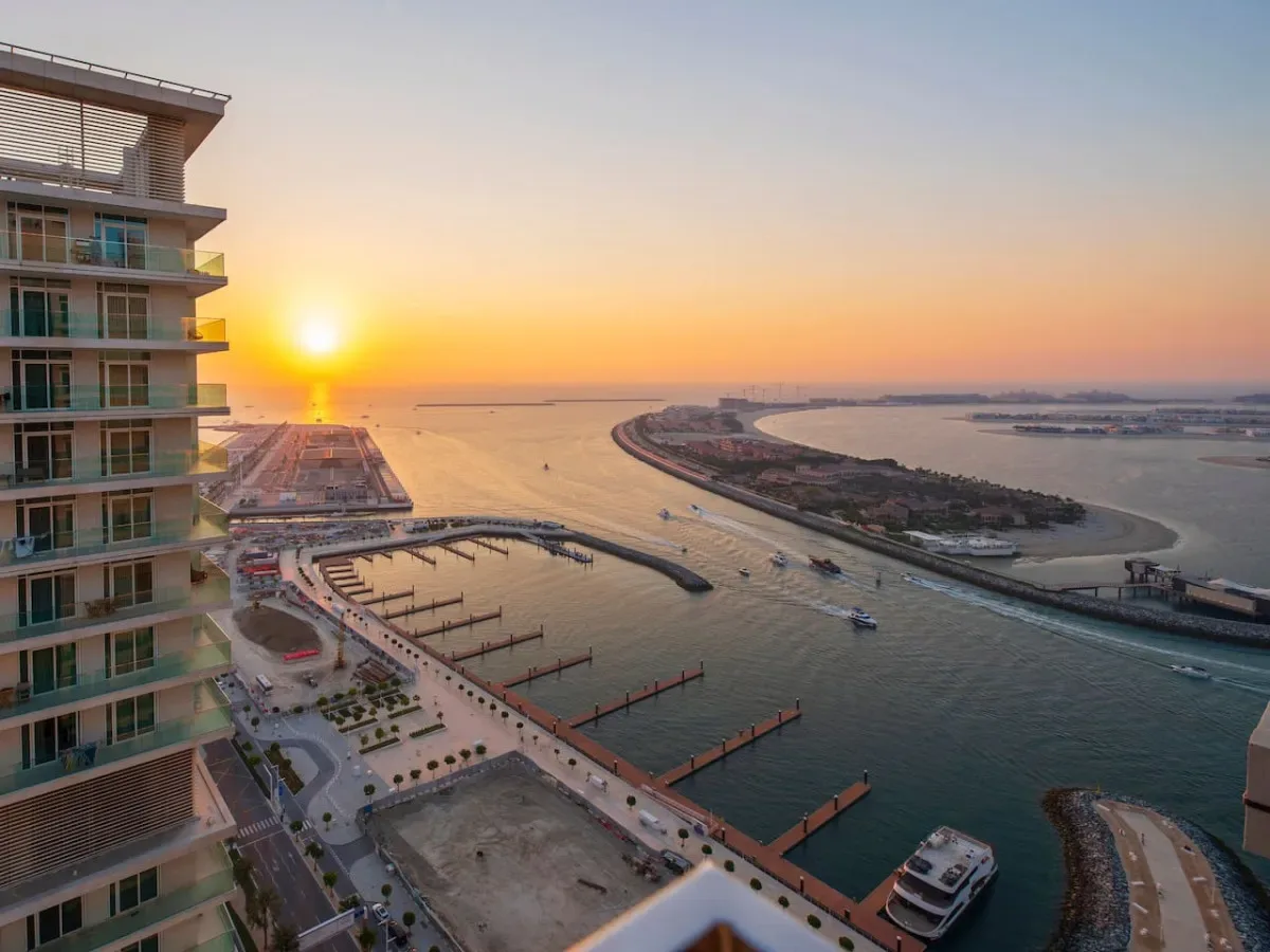 A waterfront marina and curved shoreline are visible at sunset beside a modern high-rise.