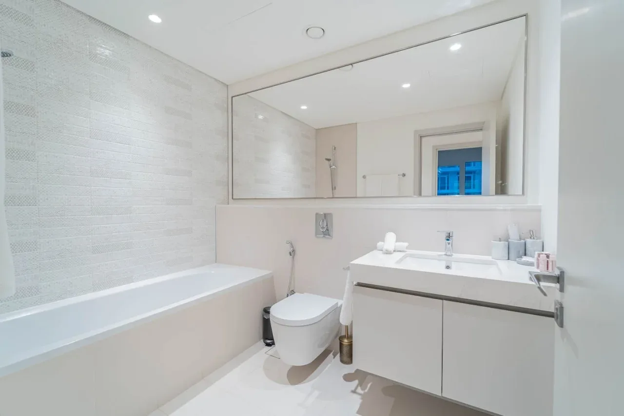 A bright bathroom with a bathtub, toilet, and sink beneath a large mirror.
