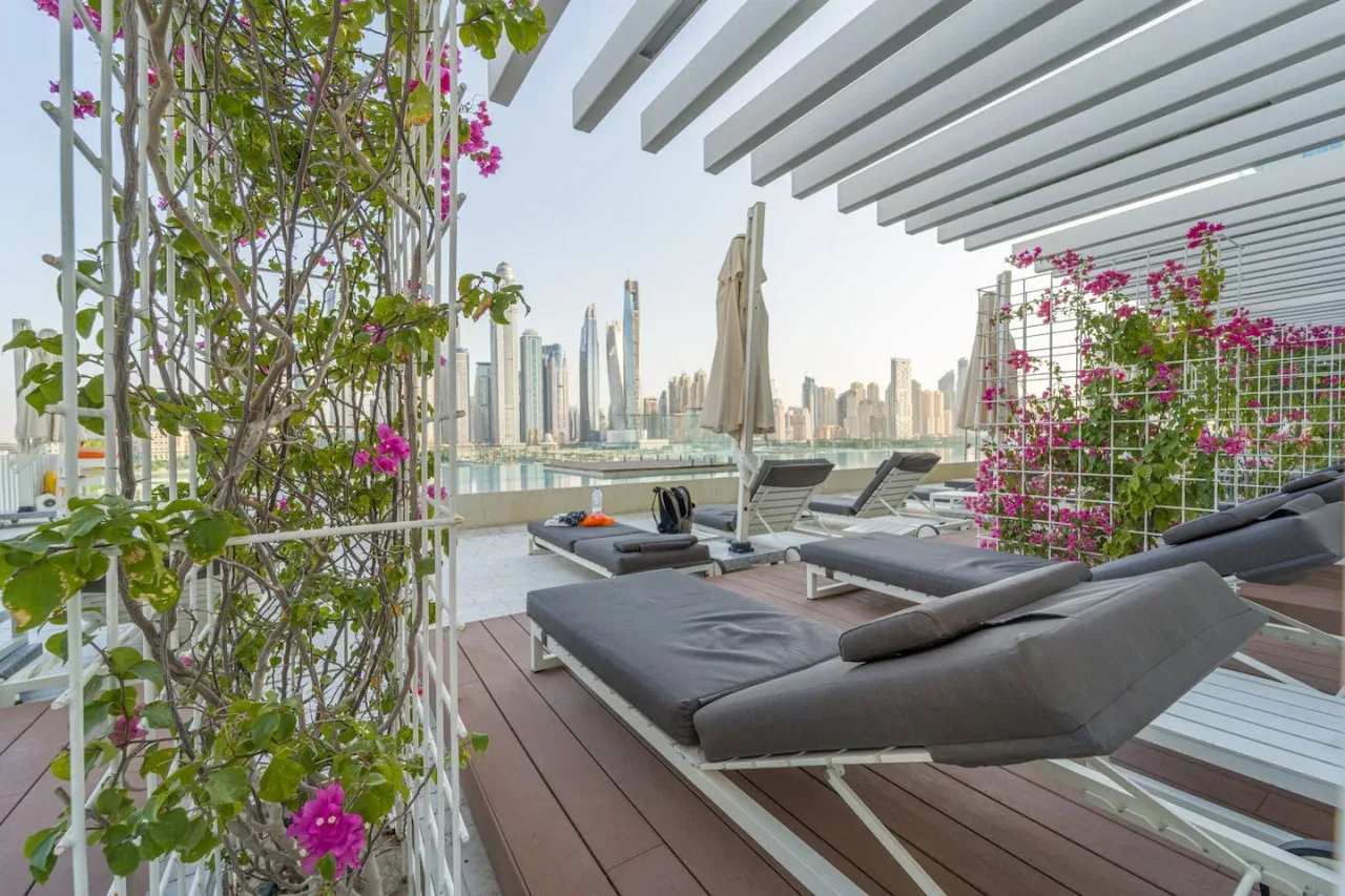 A rooftop terrace with cushioned seating, flowering plants, and a city skyline.