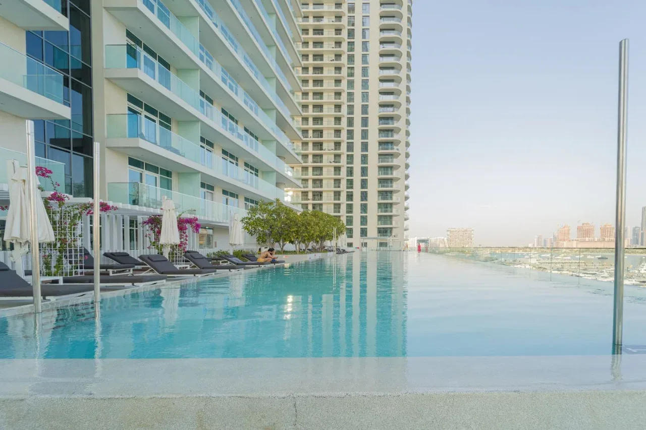 A rooftop swimming pool beside a high-rise building, with lounge seating along the water.