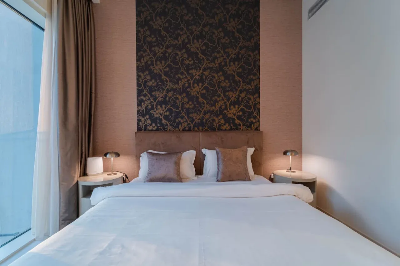 A bedroom with a neatly made bed and patterned wall panel behind it.