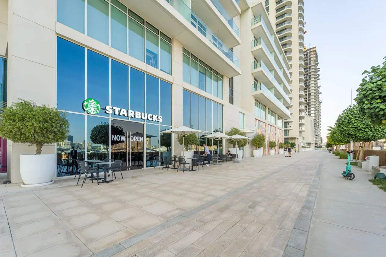 A Starbucks café with outdoor seating along a paved walkway beside modern buildings.