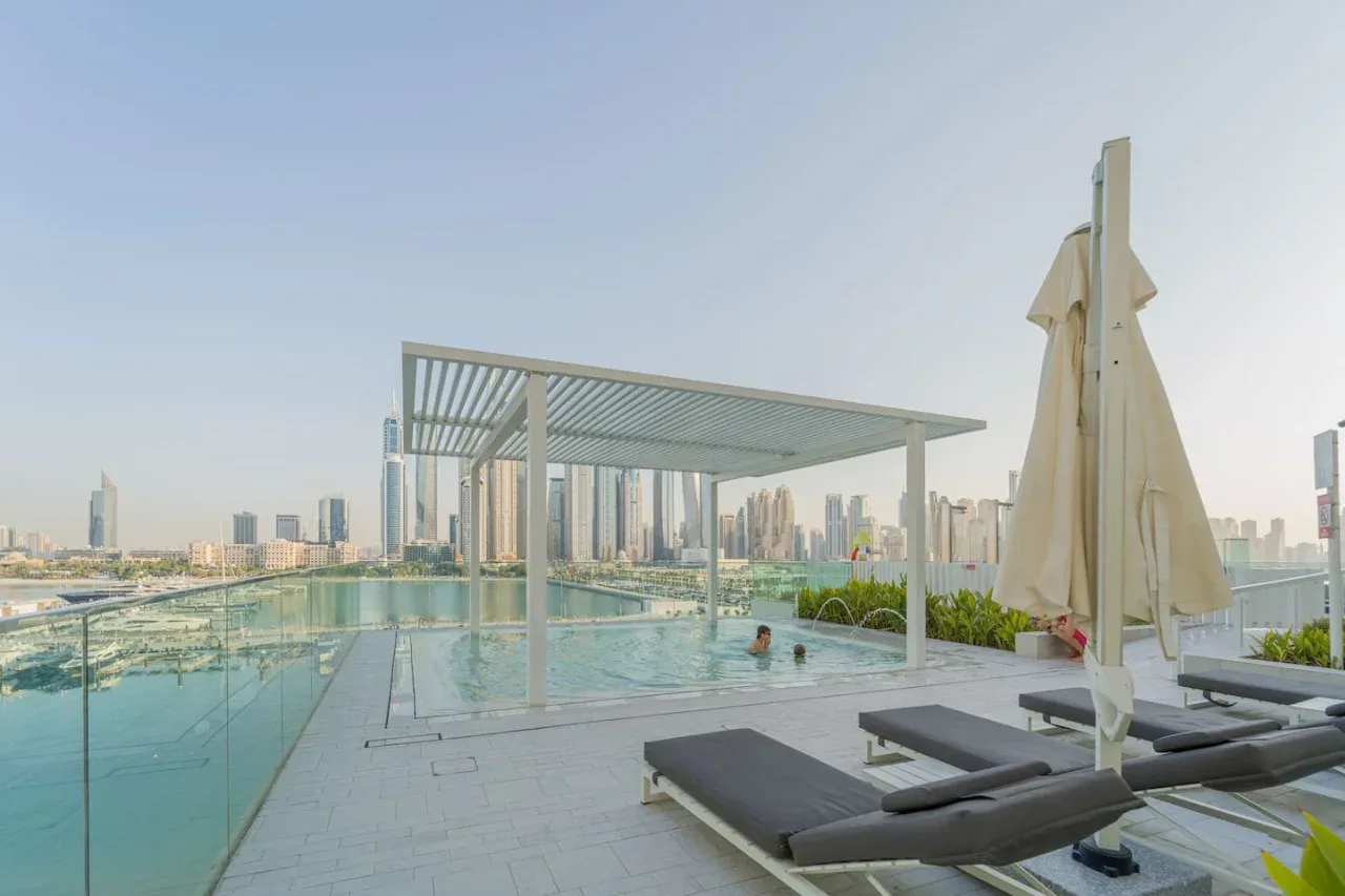 A rooftop pool beside a shaded seating area overlooks the city skyline.