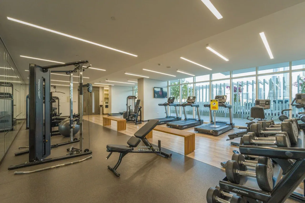 A bright gym with exercise machines, treadmills, and large windows.