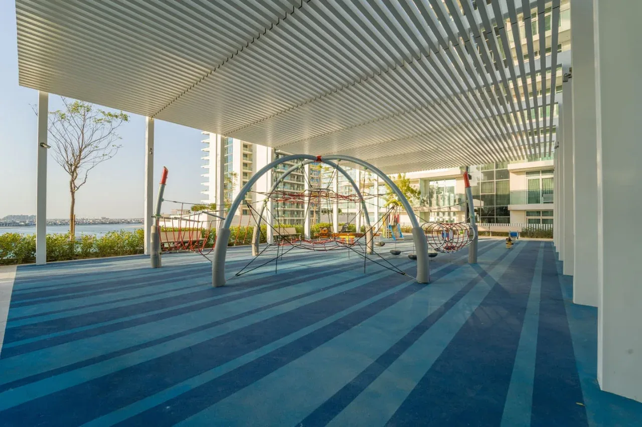 A covered outdoor play area has climbing equipment on a blue striped surface.