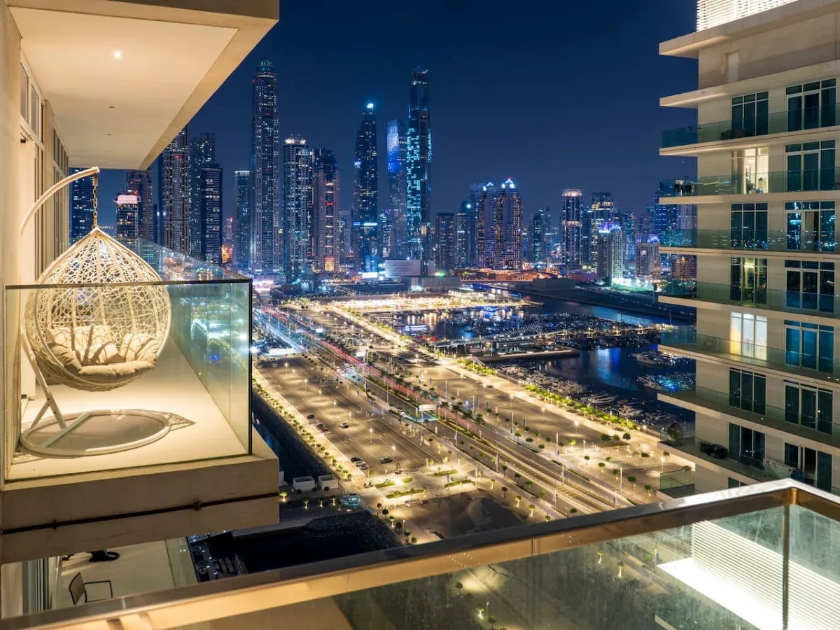 A balcony overlooks a brightly lit city skyline and multilane roads at night.