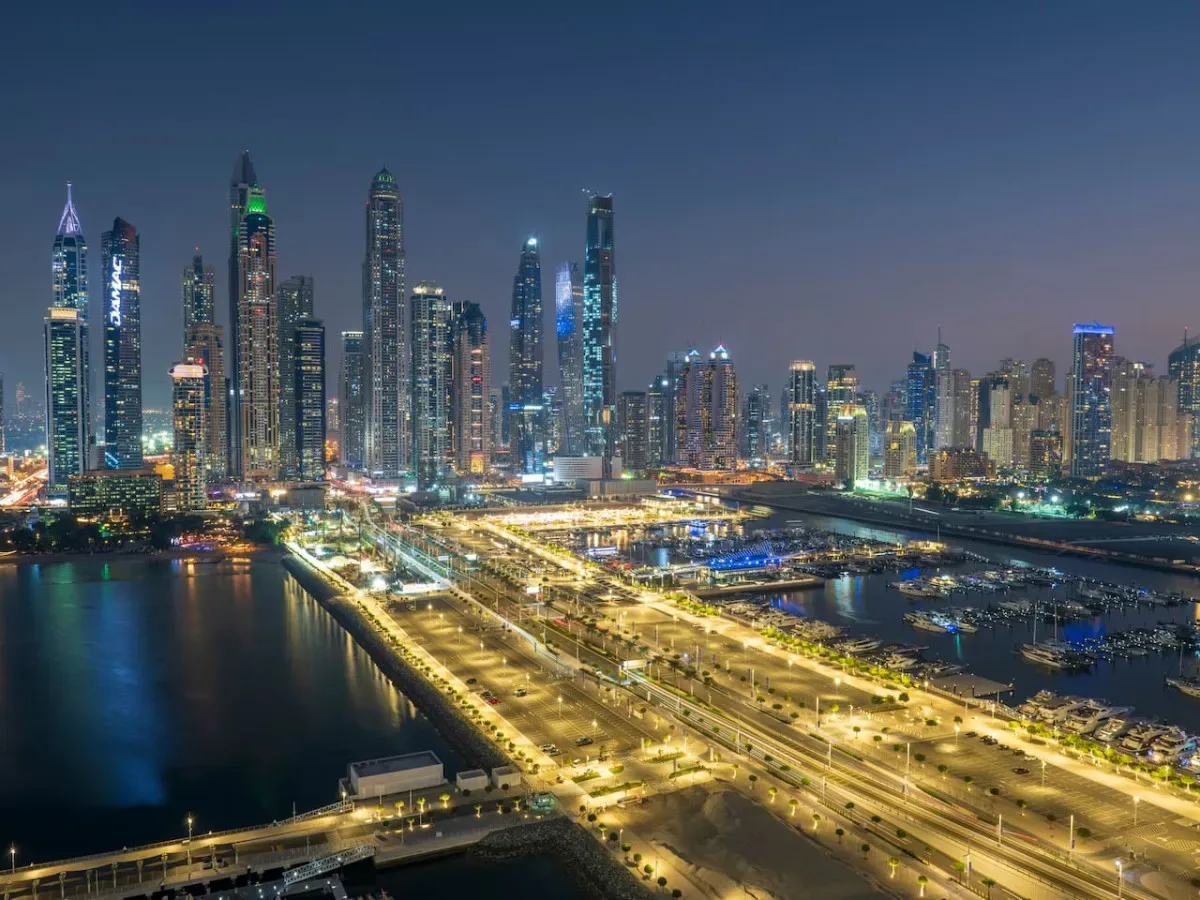 A nighttime city skyline with illuminated high-rise buildings and roads beside the water.