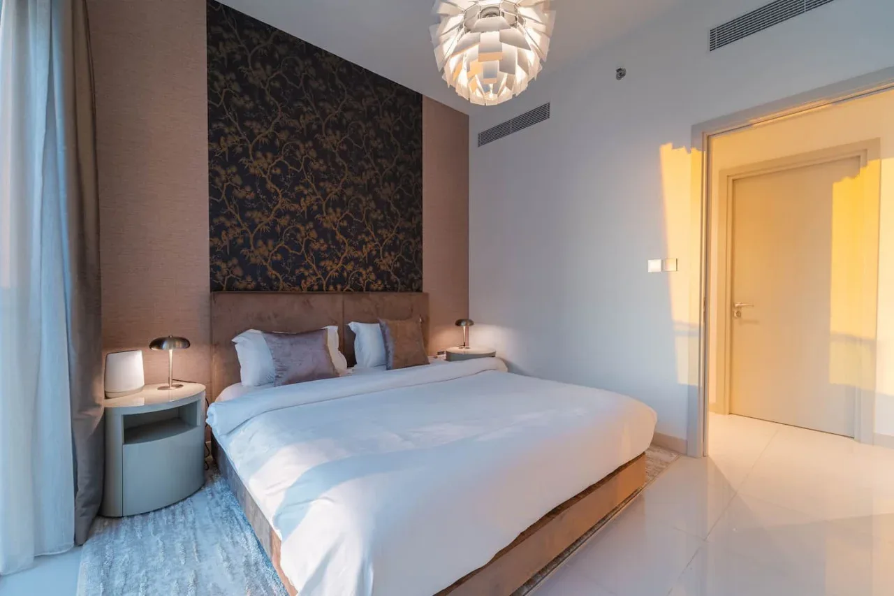 A bedroom with a large bed, bedside tables, and patterned wall decor.