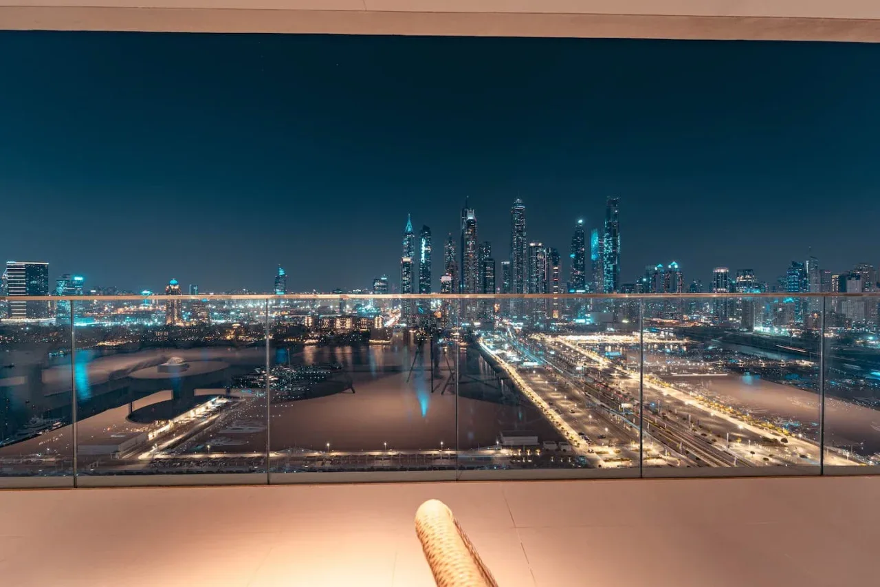 A balcony overlooks a brightly lit city skyline and roads at night.