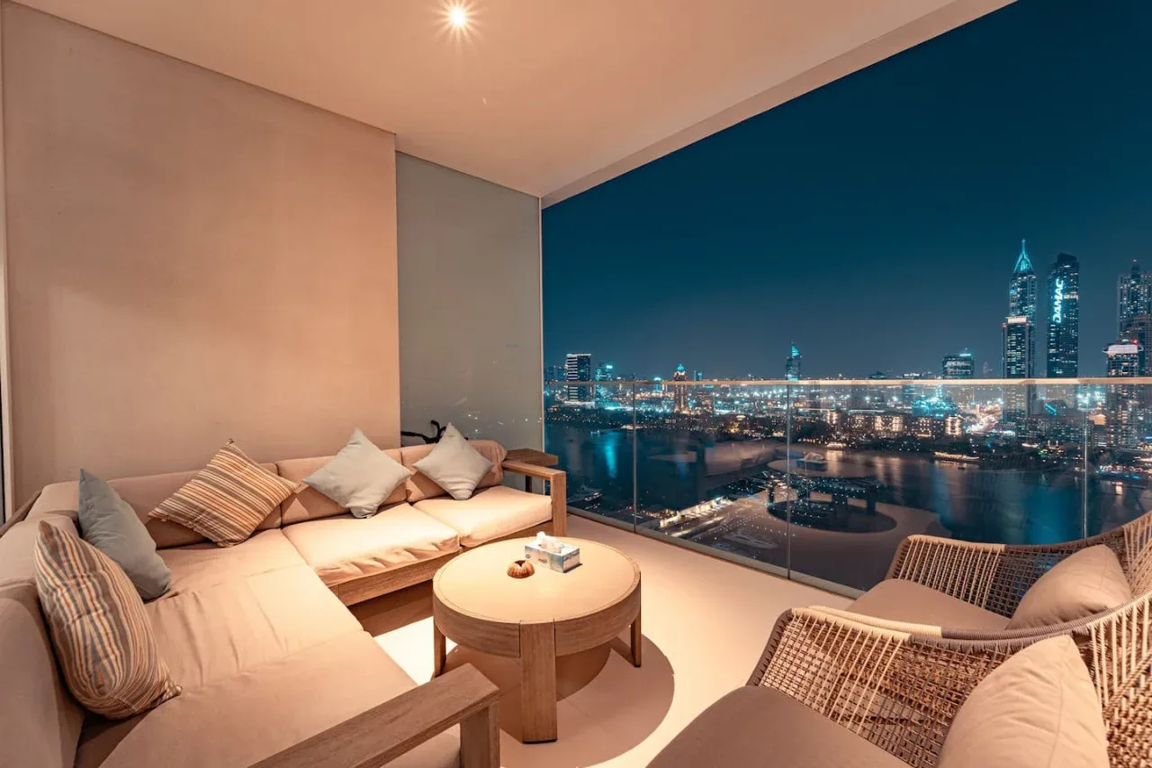 A living room with lounge seating and a nighttime city view through large windows.