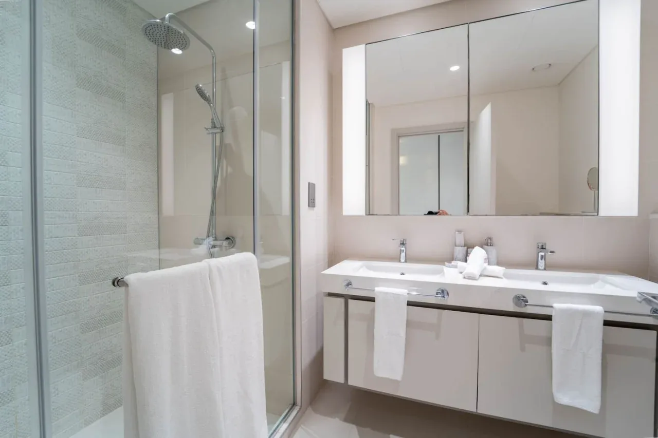 A bright bathroom with a glass-enclosed shower and a double-sink vanity.