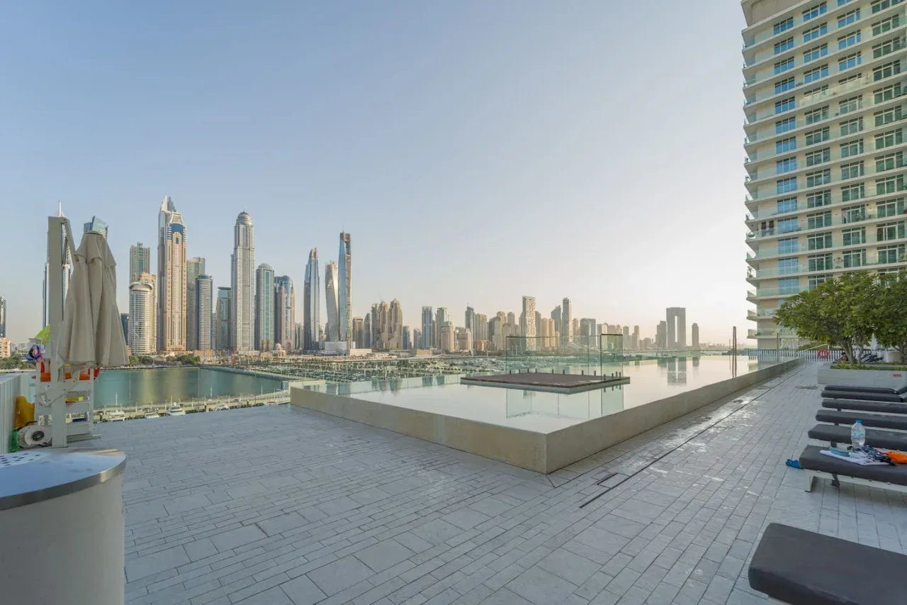 A rooftop terrace overlooks a waterfront skyline, with seating along the paved deck.