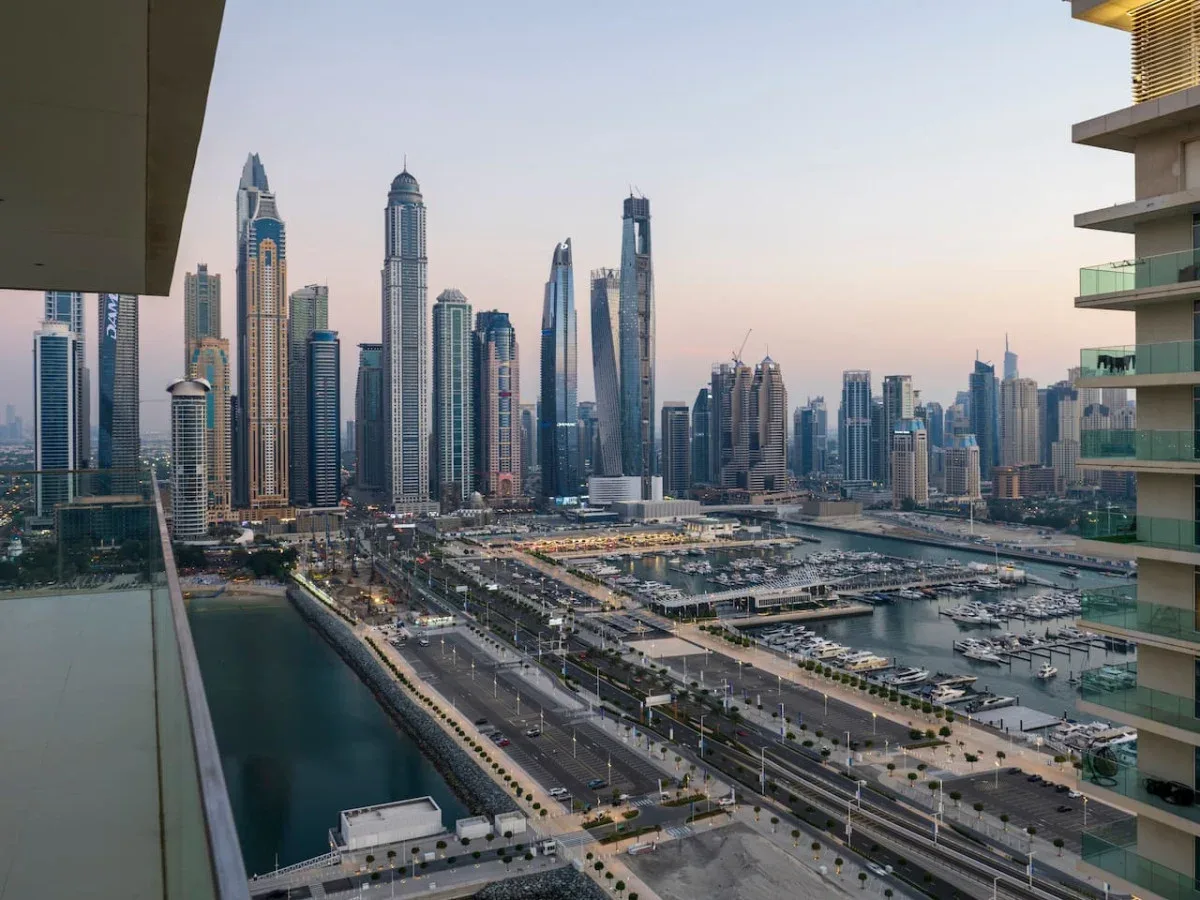 A waterfront city skyline rises above roads and a marina at dusk.