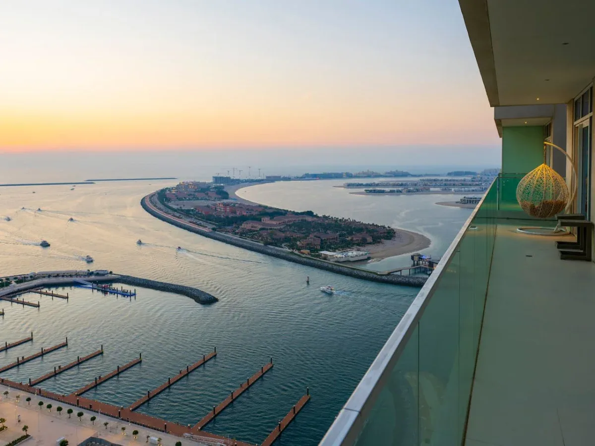 A balcony overlooks a waterfront marina and a curved shoreline at sunset.