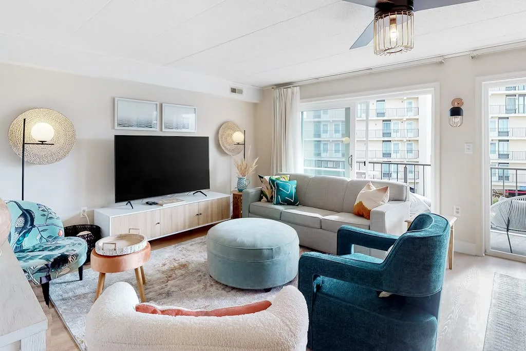 A bright living room with seating arranged around a television and large windows.